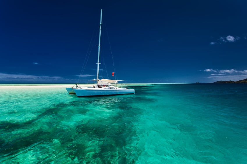 White catamaran in shallow tropical water with green snorkeling reef